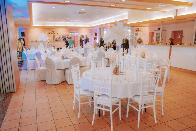 Elegantes Hochzeitsbankett mit weiß eingedeckten runden Tischen und Stühlen in festlichem Saal.