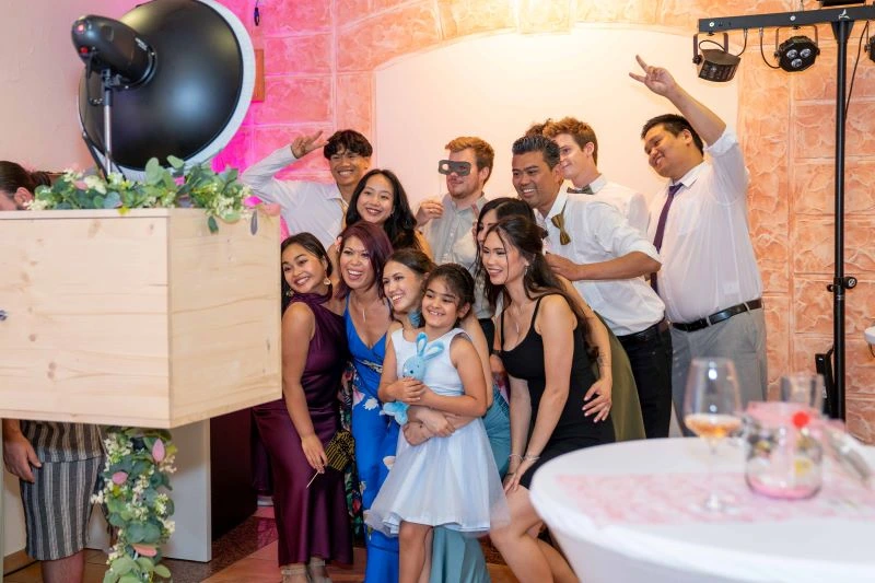 Gruppe von Menschen posiert fröhlich für ein Foto auf einer Feier, mit Dekorationen und Beleuchtung im Hintergrund.