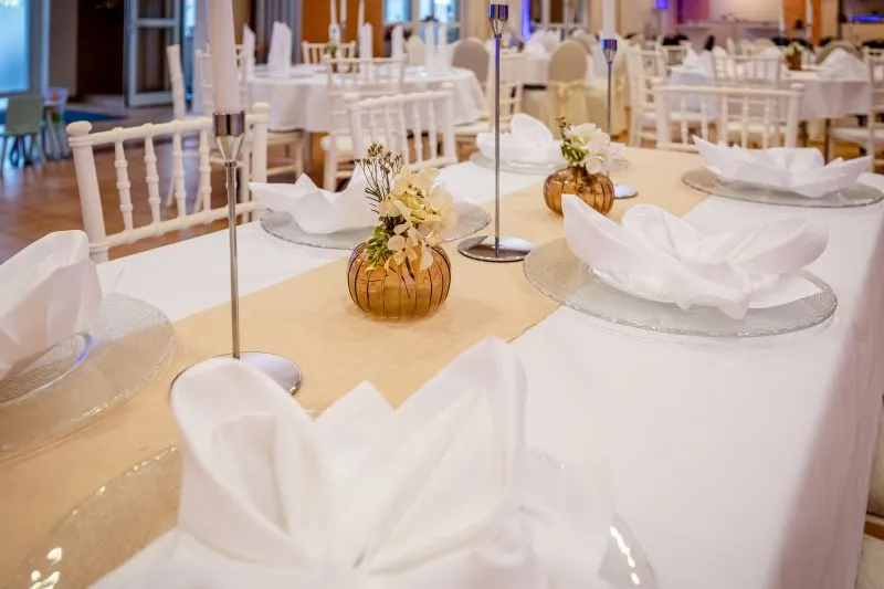 Elegante Hochzeitstafel mit weißen Servietten, Glasuntersetzern und dekorativen Blumenvasen in stilvoller Atmosphäre.