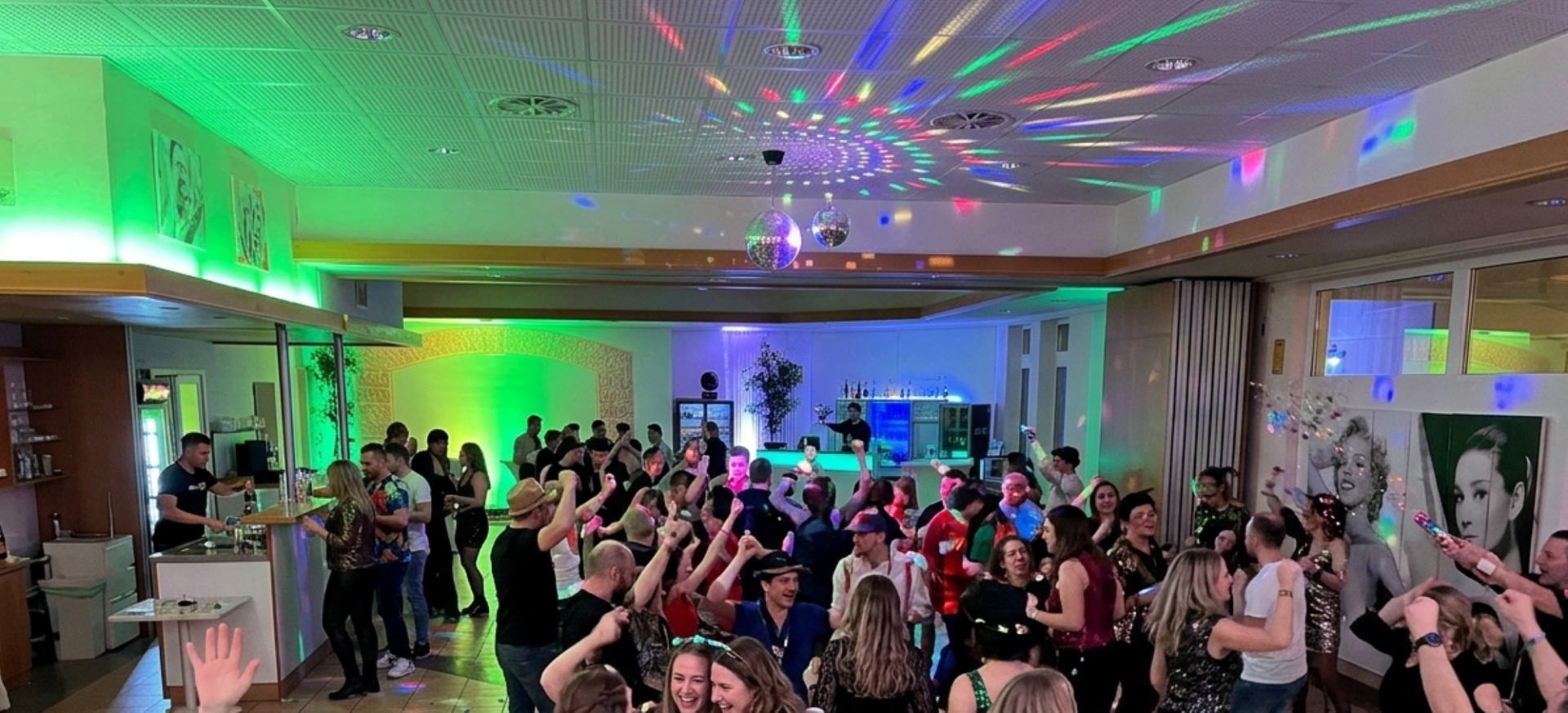 Fröhliche Party mit Tanz, Disco-Lichtern und Gästen in festlicher Stimmung in einem bunt dekorierten Veranstaltungsraum.