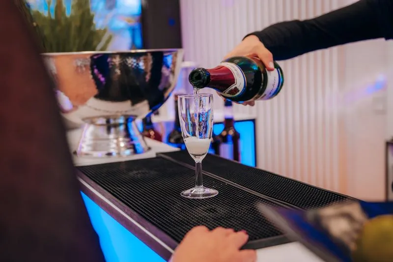 Ein Kellner schenkt Champagner in ein Glas bei einer eleganten Veranstaltung an einer beleuchteten Bar ein.