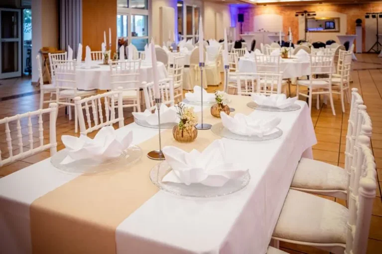 Elegantes Hochzeits- oder Event-Dekor mit weiß gedeckten Tischen, Blumenarrangements und Kerzen für eine stilvolle Feier.