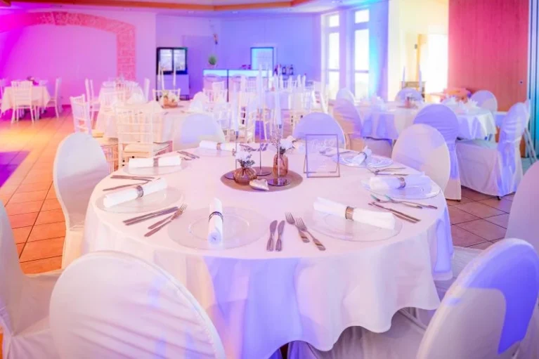 Elegante Hochzeitstischdekoration mit weißen Tischdecken, Blumenarrangement und Besteck in einem festlich beleuchteten Bankettsaal.
